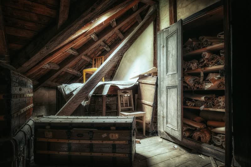 Vollgestellter Estrich mit alter Holztruhe, Stühlen und Regalen unter dem Dach